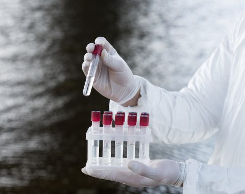 partial view of water inspector in protective costume holding test tubes